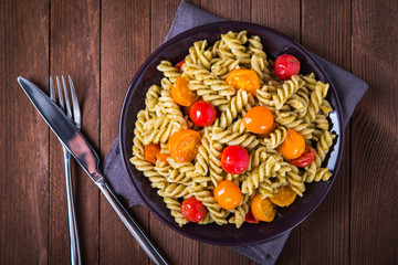 Fusilli pasta salad with pesto genovese and colorful tomatoes on dark wooden background top view. Italian cuisine. Delicious meal.