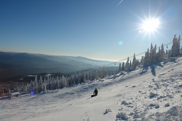 Lonely Snowboarder on the white piste with sun reflections and ski lift and beautiful panoramic...