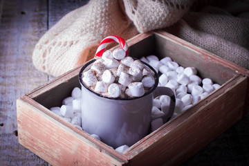 Hot chocolate with marshmallows and candy cane in a gray ceramic cup in wooden box on rustic background. Christmas concept