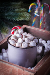 Hot chocolate with marshmallows and candy cane in a gray ceramic cup in wooden box on rustic background. Christmas concept