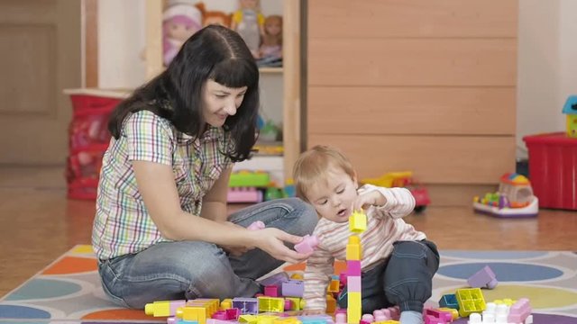 Cute little boy and mother playing with toy blocks at home, in the room, sitting on the floor.