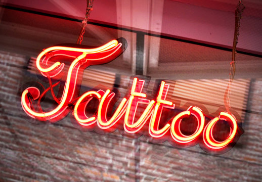 Red Illuminated Tattoo Sign In A Shop Window. Close-up.