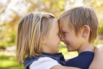 Young brother and sister nose to nose in a park, side view