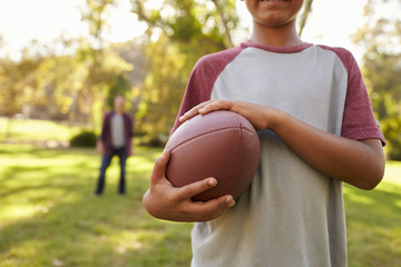 Boy holding football in park, crop, dad in background - Powered by Adobe