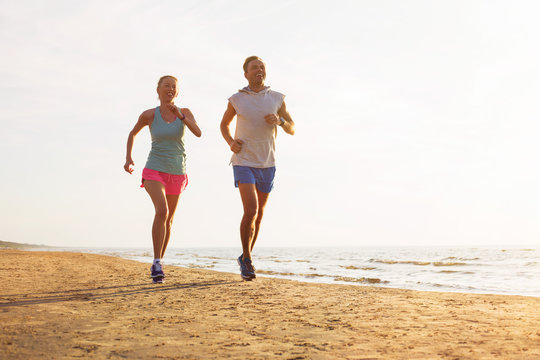Happy fitness couple running on the beach