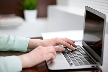 Business woman hands in a green blouse sitting at the desk in the office and typing on the laptop .
