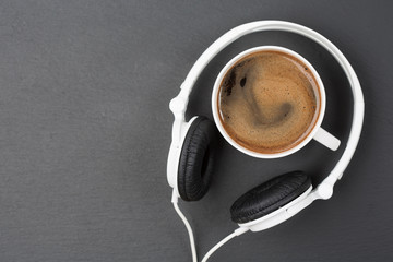 Cup of coffee and white Headphones, top view. Black table