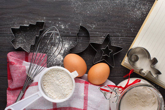 Christmas background with cookies cutters, flour, spices and eggs on old rustic wooden table, top view with copy space. Holiday concept