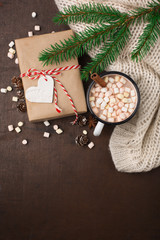 Cup with homemade Christmas hot Chocolate drink, Marshmallows and Holiday Gift on dark background. Winter time concept. Flat lay, top view