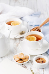 Fototapeta na wymiar Two cups of hot black tea, lemon, homemade cookies and honey on white rustic wooden background. Breakfast concept.
