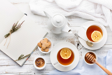 Obraz na płótnie Canvas Two cups of hot black tea, lemon, homemade cookies and honey on white rustic wooden background. Breakfast concept. Top view, flat lay style