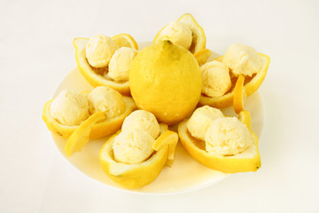 Amalfitano lemon halves filled with homemade lemon ice cream served on a white porcelain plate. An ivory colored tablecloth as background.