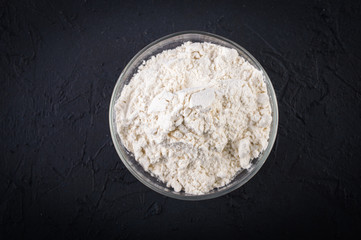 Flour in a bowl. On a black background.Top view. Flat lay.