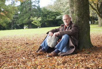 Obraz premium Portrait of a happy mature man sitting under a tree in autumn 