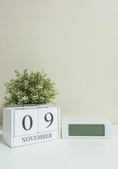 White wooden calendar with black 9 november word with clock and plant on white wood desk and cream wallpaper textured background , selective focus at the calendar