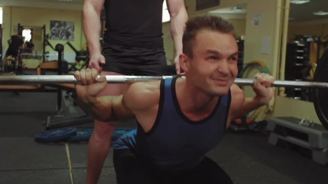 Athletes perform exercises a squats with a barbell in the gym with the trainer