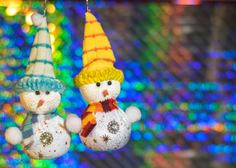 Two toy snowman on the background of colorful bokeh.
