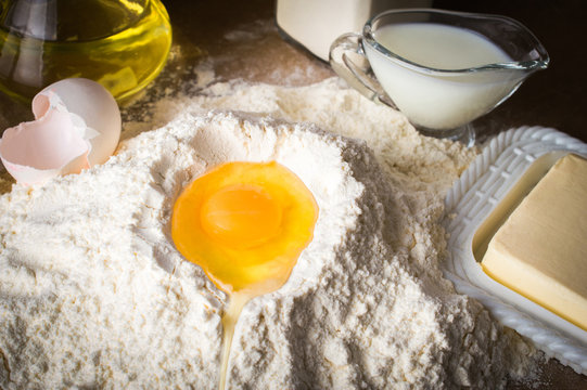 Egg on a pile of flour. Ingredients for the dough. On parchment. On wooden background.