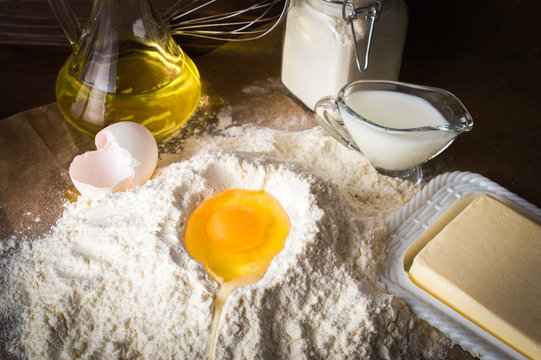 Egg on a pile of flour. Ingredients for the dough. On parchment. On wooden background.
