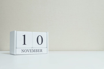 Closeup white wooden calendar with black 10 november word on blurred white wood desk and cream color wallpaper in room textured background with copy space , selective focus at the calendar