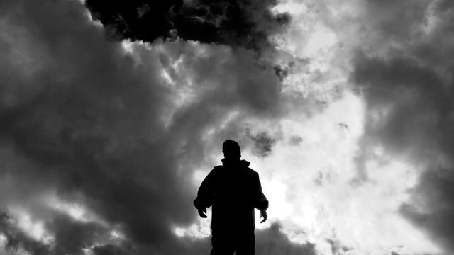 Dark and mysterious silhouetted figure stands tall looking out on cloudy day.