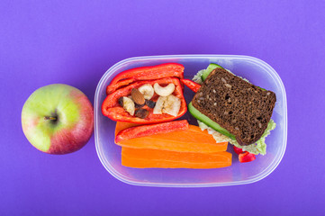 Lunch box with breakfast, an apple. On purple background.