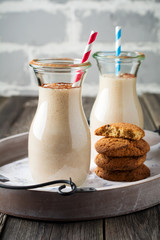 Milk vanilla smoothies with oatmeal cookies in glass jars on the old wooden background. Selective focus.