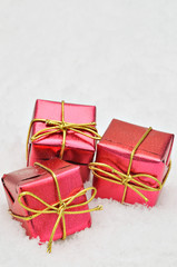 Red gift boxes on Snow background / three small red, metallic bright parcels on snow background, close up, space for text, vertical