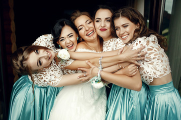 Happy bridesmaids hug bride tightly standing on balcony