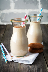 Milk vanilla smoothies with oatmeal cookies in glass jars on the old wooden background. Selective focus.