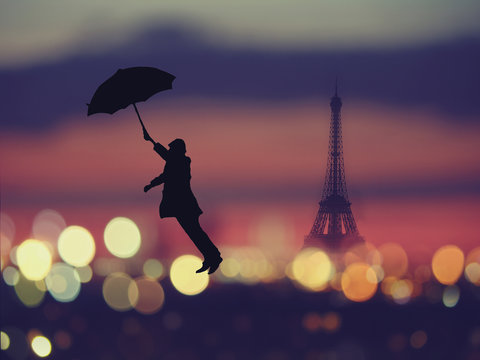 silhouette of a man holding umbrella flying  over night Paris , France with eiffel tower on a background.