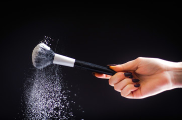 The hand holding the brush with the powder flies. On a black background.