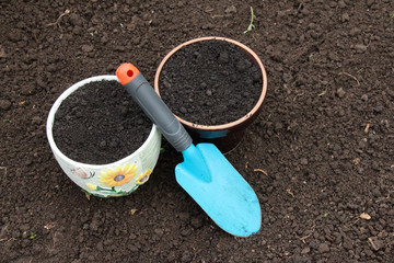 Ceramic flowerpots filled with the fresh soil for planting and a garden trowel in the polycarbonate greenhouse prepared for wintering