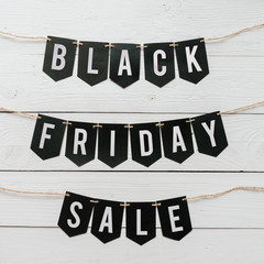 Obraz premium Black Friday Sale paper banner garland lettering hanging on white barn wood planks background. Beautiful holiday flyer.