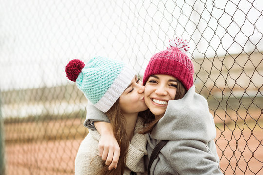 Cheerful teenage girl kissing her best female friend outdoors in winter