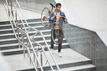 Guy in denim jacket going down the stairs holding an orange bicycle. Student with the bike  