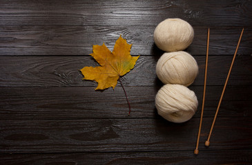 White yarn, wooden knitting needles, yellow leaves on dark table