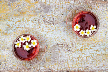 Two glass cup of tea on old wooden surface. Small white flowers.
