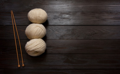 Skeins and wooden knitting needles on a  dark wooden table.