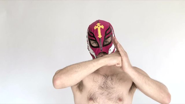 Model released man in studio wearing red lucha libre mask wrestles and challenges viewer.