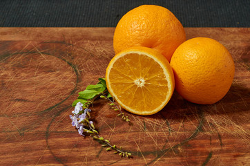 A group of oranges with a lemon and half a lime showing segments, on a wooden board with leaves as decoration.