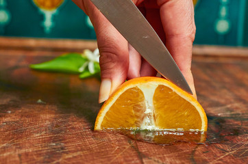 A quarter of an orange on a wooden board being sliced with a knife being held by a woman's hands.