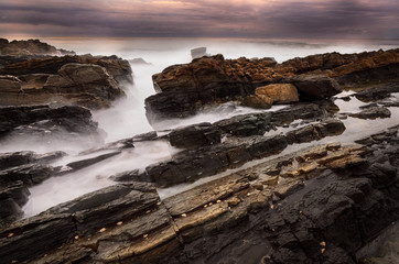 Fototapeta na wymiar Mystical rock pool on a rocky ocean coastline in the early morning on an overcast day