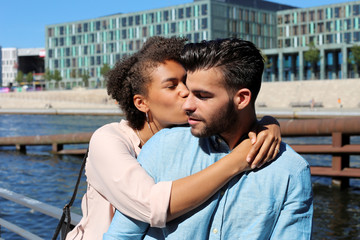 Attraktives Frau Umarmt ihren Freund und küsst Ihn auf die Wange am Fluß in der Stadt