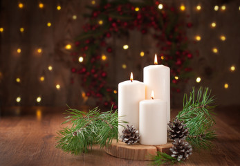 Obraz na płótnie Canvas burning candles wooden table pine branches cones background with Christmas wreath and lights