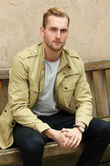Obraz premium Focused trendy man sitting down outdoors on a bench thinking. Wearing a yellow jacket.