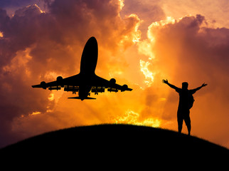 Fototapeta na wymiar silhouette man backpacker standing raised up arms achievements successful and celebrate with airplane flying take off from runway in sunset