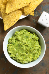 Avocado dip or guacamole in bowl with corn tortilla chips, photographed overhead with natural light (Selective Focus, Focus on the avocado dip and the tortilla chip on the top)
