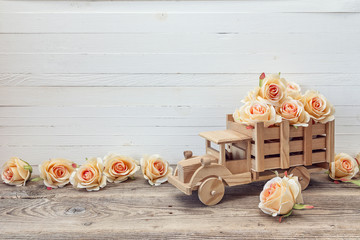 Wooden toy truck with peach roses flowers in the back on a white