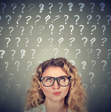 Thinking woman looking up at many questions marks above head